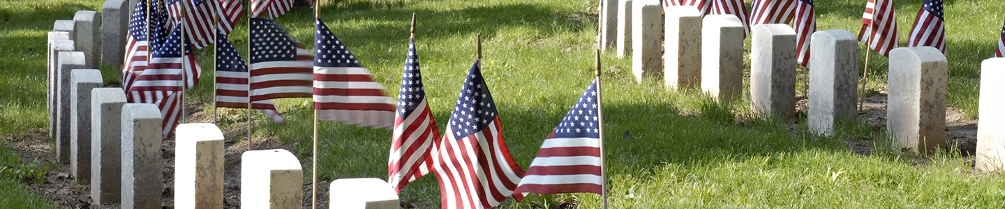 rows of American flags stand beside cemetery headstones