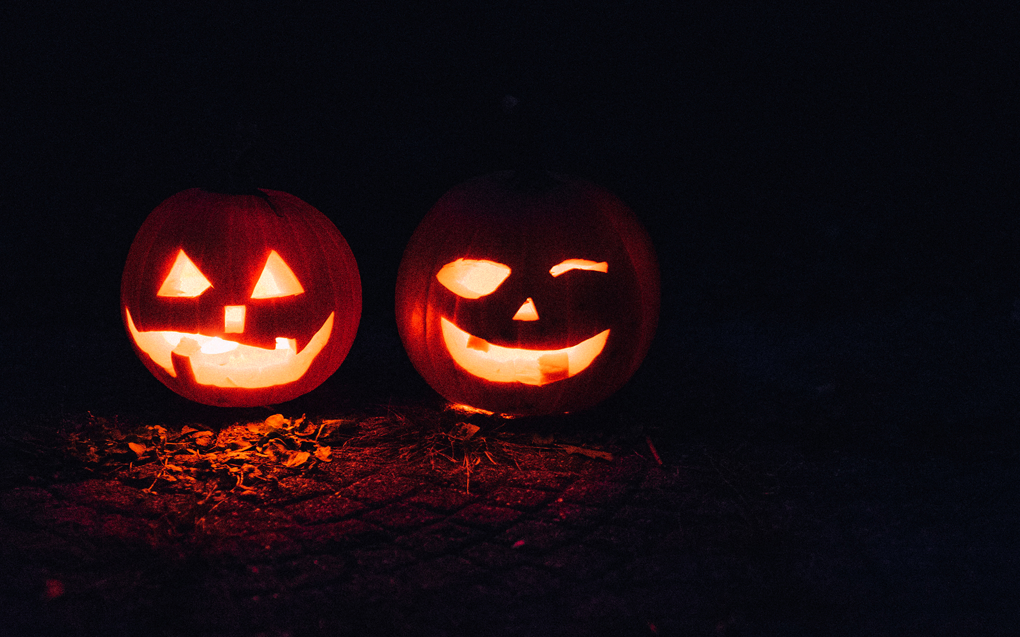 a pair of lighted carved pumpkins glow at night