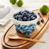 white ceramic bowl with blue flower pattern holding blueberries sitting on wooden cutting board with wooden spoon and limes sitting next to it