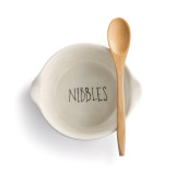 top view of white ceramic dish reading Nibbles in black letters at bottom with wooden spoon laying across top