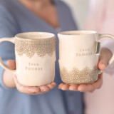 two women holding cream ceramic mugs with tan lace detailing which read 'true friends'