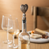 bottle stopper topped silver carving of heart in wine bottle sitting on table in front of wine glasses and cheese plate