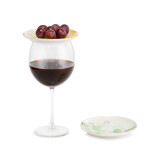 Two yellow, green, and white ceramic floral print wine appetizer plates. One placed on a glass of wine topped with grapes.