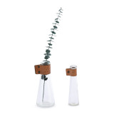 Two glass bud vases with leather straps. Filled with a single greenery stem.