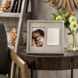 A light gray frame with a tan textured background. Displays a picture of a father and a baby. Frame states "Love my dad". Placed upon a hardwood side table beside a striped chair.