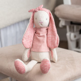 A plush pink and cream linen bunny, displayed sitting on a tan ottoman.