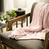 A light pink chenille throw blanket draped over an armchair in a living room setting.