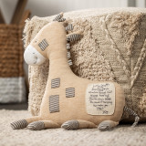 A tan textured pouf ottoman with a tan and striped giraffe leaning against it. Pictured in a baby nursery.