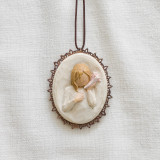 Close view of cream round pendant with carved in image of blonde girl figurine with seashell up to her ear