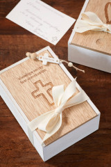 Two white and light wooden keepsake boxes with messages engraved, and tied in a cream bow, placed on a wooden table with a white handwritten note.