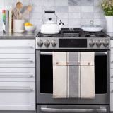 A cream and gray button loop infinity towel, shown in a kitchen setting hanging from an oven handle.