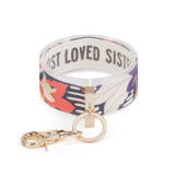 An expanded purple and pink floral print wrist strap with gold metal accents. Inside reads "most loved sister".
