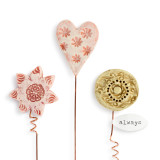 A close up image of a set of three textured gardening picks - a light pink heart, a yellow flower with a white tag that reads always", and a light red flower. Each on copper wire."