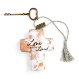 An orange and white floral print Artful Cross that reads "love and be loved". With a bronze key and a silver tassel.