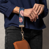 A woman wearing black jeans, a blue blouse, and a blue floral print wrist strap attached to a small leather bag.