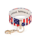 An expanded American flag print wrist strap with gold metal accents. Inside reads proud, brave, & free"."