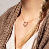 A cropped close image of a woman in a cream blouse and brown sweater with a delicate circle necklace.