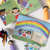 A five piece wooden puzzle and a board book both with a multicultural and rainbow theme. The puzzle says "The world needs its rainbows. Hold hands and be proud!". The items are on a light wood surface with a jar of colored pencils.