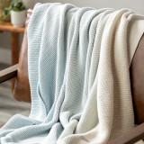 A cropped, close up image of a brown leather chair, topped with a blue and white ombre throw blanket.