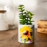 A white ceramic planter with an image of a watercolor sunflower. The planter has a fake green succulent inside, displayed on a wood table setting.