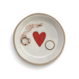 A round ceramic treasure keeper dish with a red heart and a tan textured rim. The dish has a ring and necklace inside.