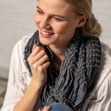 A cropped image of a woman in a white blouse wearing a dark gray textured infinity scarf.