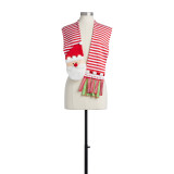 A red and white striped scarf with red and green fringed ends, white pom poms, and a felt Santa face. Placed on a black and white mannequin.