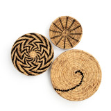 Set of three round woven wall art baskets with black details woven into the designs.