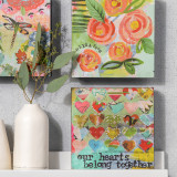 Three different square wall art pieces with different colorful images and encouraging words, set next to a couple of cream ceramic vases.