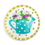 A circular clear glass plate with a yellow and white striped edge, and a blue polka dotted water pot filled with flowers.