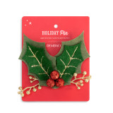 Green holly shaped fabric lapel pin embellished with red berries and gold stems, attached to packaging.