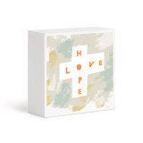 A small white box artwork of the words "Hope and Love" in a white cross shape against a pale abstract background, displayed angled to the right.