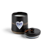 A round black ceramic poured candle with a tan textured base, a lid and a white raised heart on the front with the image of a blue butterfly, displayed with the lid off and to the side.