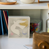 A small white square wall art with an illustration of a white dove displayed on a white desk with other supplies.