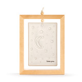 A cream ceramic plaque with the moon and stars and the saying "love you" suspended inside a light wood open frame.