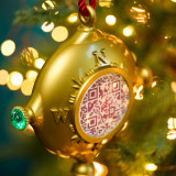 A gold plastic compass shaped ornament with a QR code in the center hanging on a lit Christmas tree. A gold plastic compass shaped ornament with a QR code in the center hanging on a lit Christmas tree.