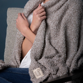 Close up of a woman wrapping a taupe colored Giving blanket around her shoulders.