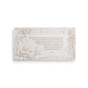 White plaque with palm trees and two people with a donkey carved in - light black religious quote centered