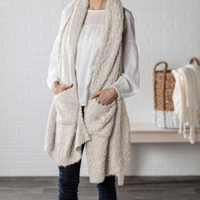 A woman in a white blouse and dark denim jeans, wearing a cream colored "Giving Shawl".