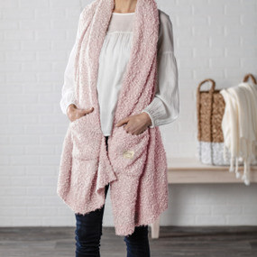 A woman in a white blouse and dark denim jeans, wearing a light pink "Giving Shawl".
