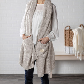 A woman in a white blouse and dark denim jeans, wearing a taupe "Giving Shawl".