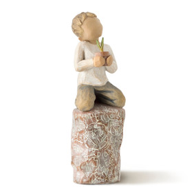 Front view of kneeling boy figure in cream shirt and blue jeans holding green potted plant on tall rock carved with words and organic imagery