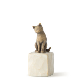 Figure of brown cat with tilted head perched atop a cream colored rectangular pedestal, facing front