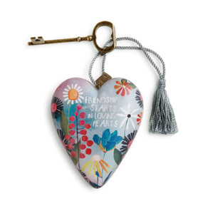 A heart shaped floral sculpture that says "Friendship Starts In Loving Hearts" with a silver tassel and metal key attached.