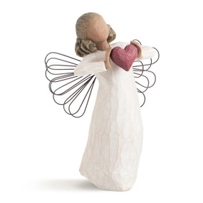 Front view of standing female angel with wire wings and darker skin and hair in cream dress, holding large red heart up to chest