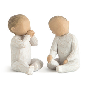 Two seated baby figures, both in cream onesies, one with hands up to mouth, one with hands in lap