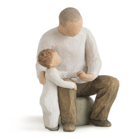Front view of male figure seated on rock in cream shirt and dark pants, holding toddler standing next to him