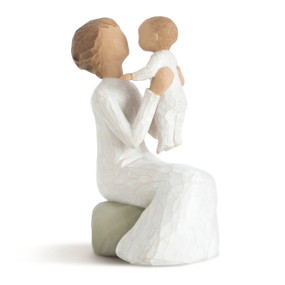 Front view of female figure in cream dress, seated on gray rock, holding baby up in the air