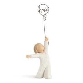 Front view of standing child figure in cream dress, holding wire balloon with word hope" written in wire inside of it"
