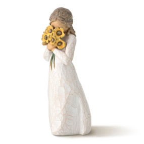 Front view of standing figure in cream dress with long hair tied back, holding large bouquet of yellow sunflowers to face